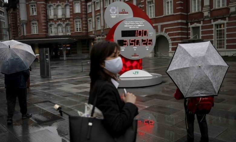 Seorang perempuan dengan masker di wajahnya berjalan di depan jam penghitung mundur 100 hari menjelang Olimpiade Tokyo 2020 di Tokyo, Jepang, Rabu (14/4/2021). Foto : Antara/Reuters/Issei Kato/wsj